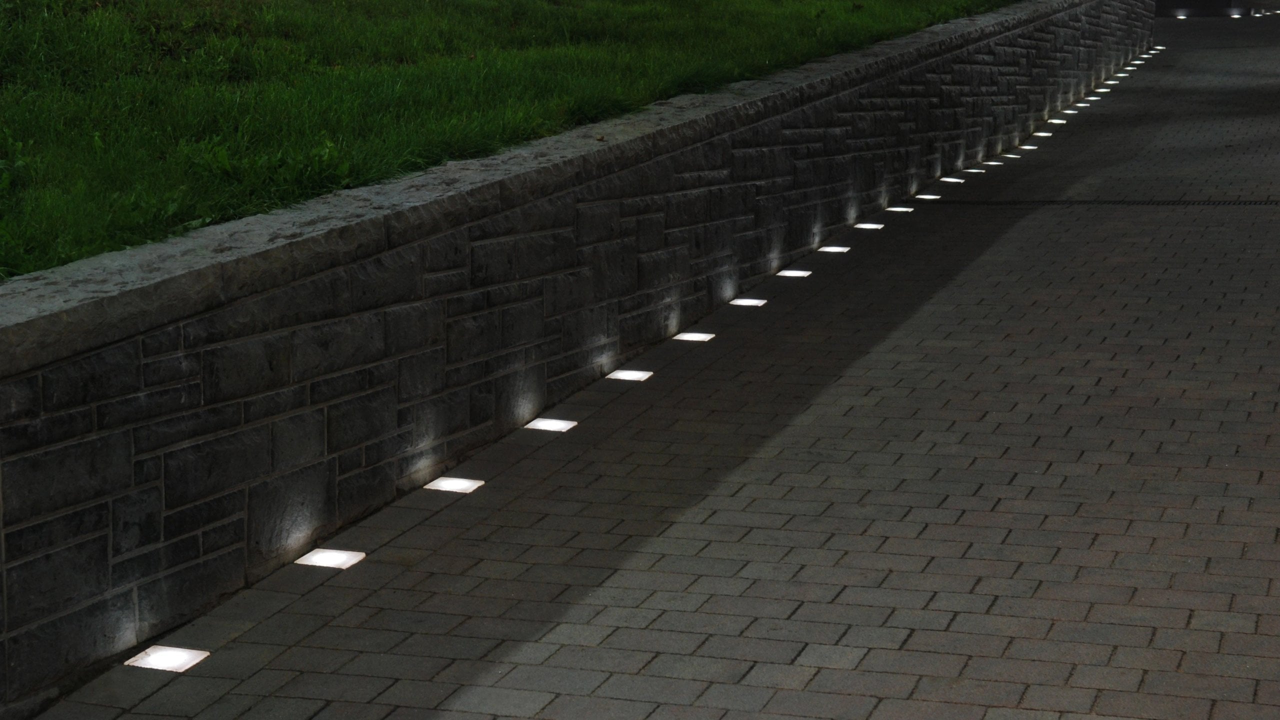 Paved path at night along a retaining wall, Beckstone LED Paver Lights lining the edge of the path