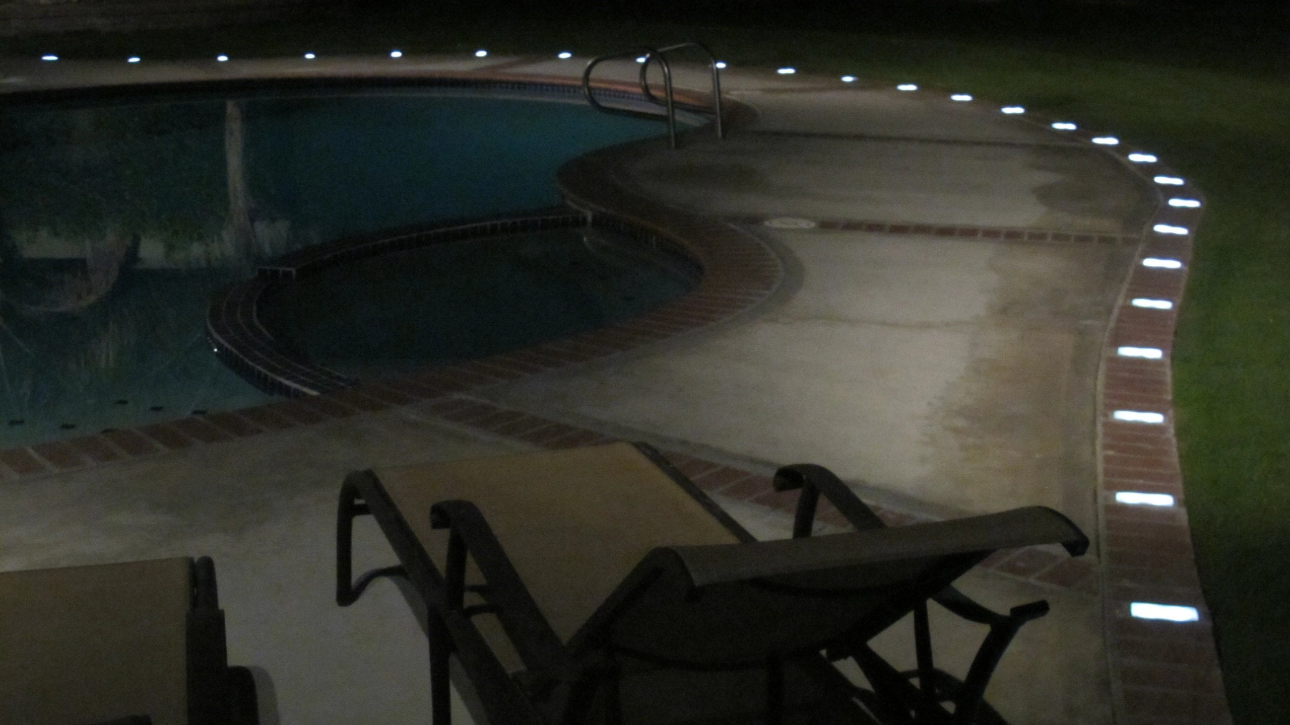 Beckstone LED Paver Lights lining the edge of a swimming pool at night