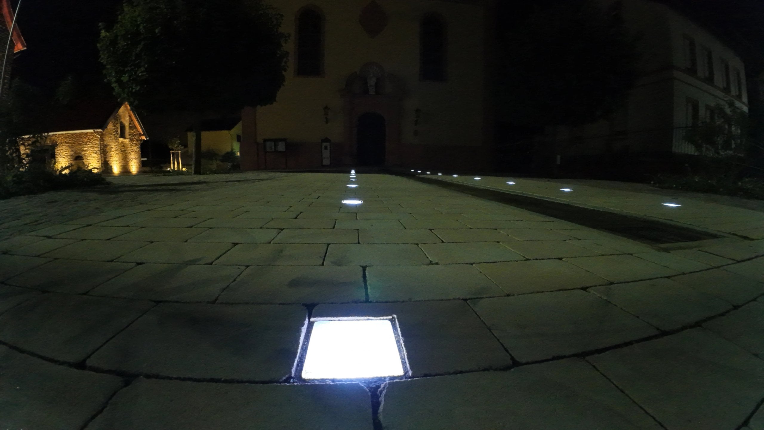 Lightstone LED-Pflasterstein in einer Plattenfläche vor einer Kirche bei Nacht
