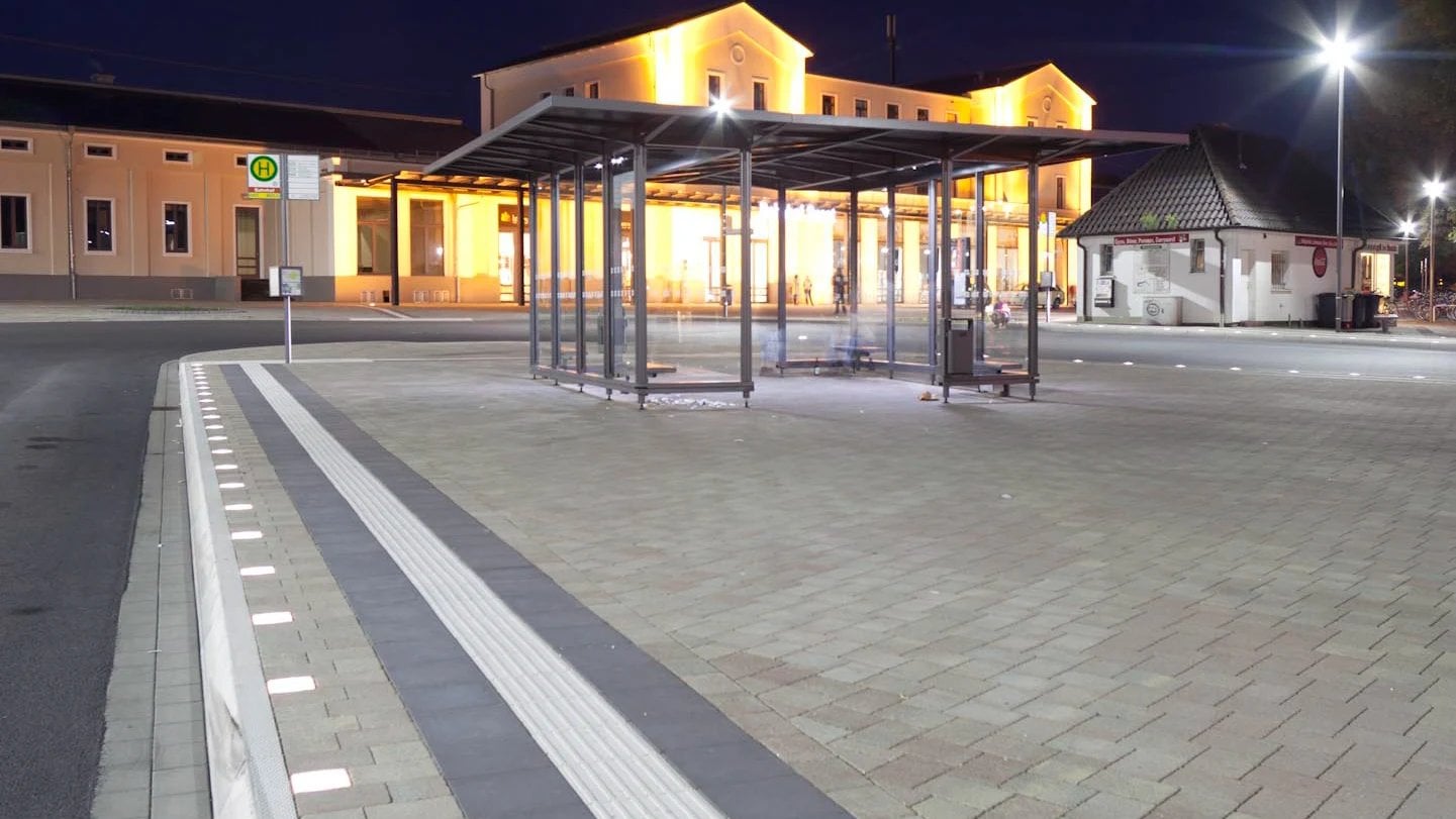 Public transport stop on a station forecourt at night, Paver Lights tracing the platform edge