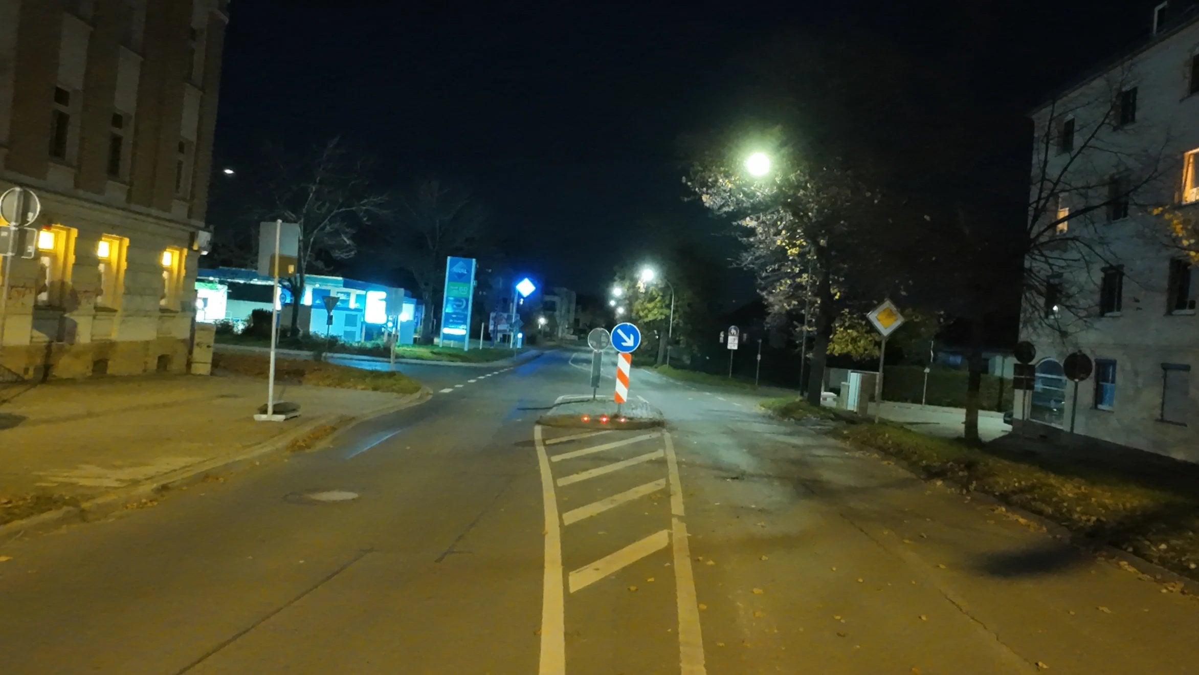 Straße mit Verkehrsinsel bei Nacht, ein rot-weißes Warnzeichen markiert die Spitze