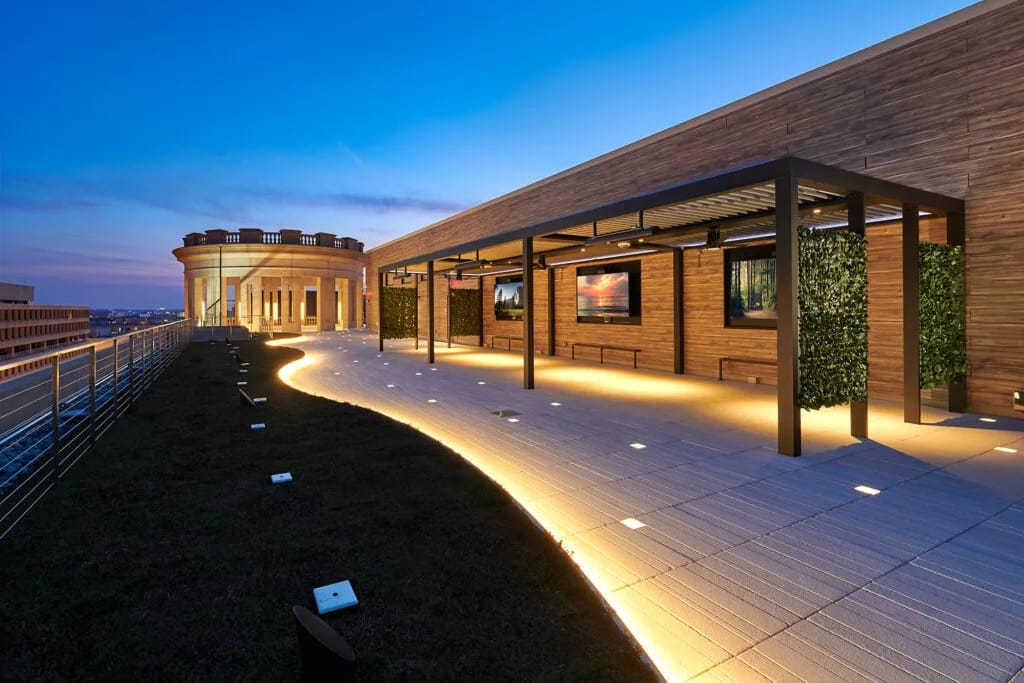 Roof terrace at a timber building at dusk, illuminated stones in the slab paving