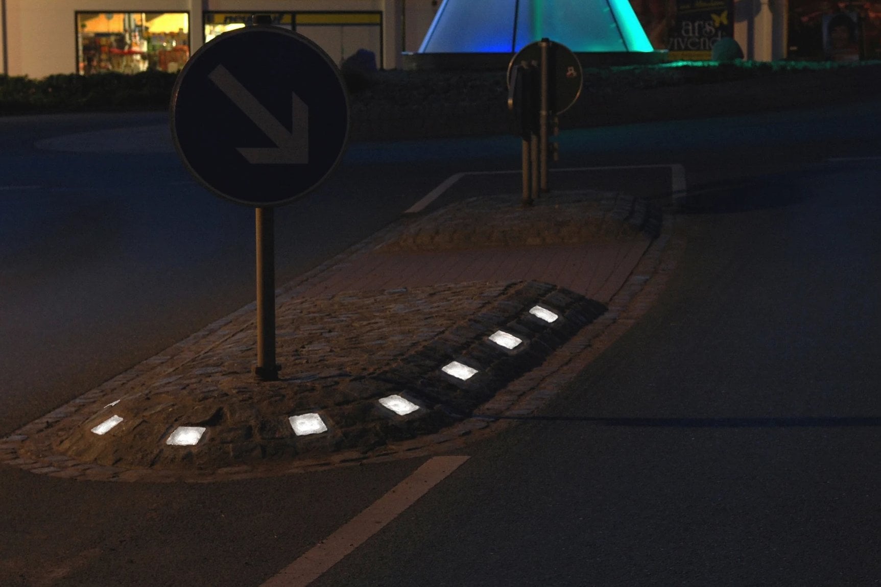 Traffic island at night with a keep right sign, illuminated stones at its nose