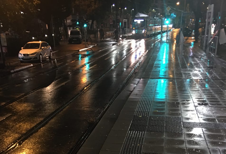 Haltestelle bei Nacht und Regen mit spiegelnden Scheinwerfern und Lichtreflexen