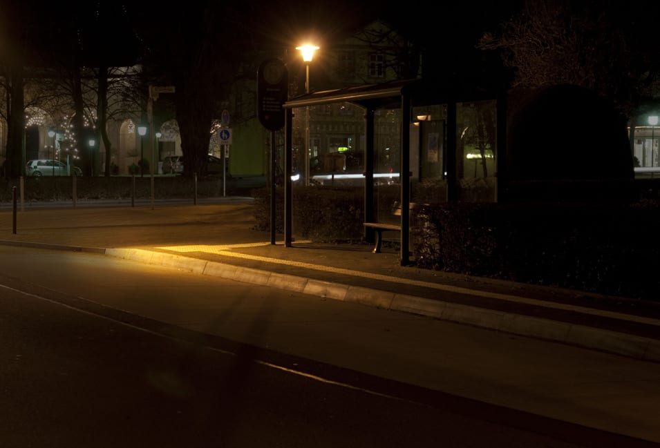Haltestelle bei Nacht, eine einzelne Mastleuchte erhellt nur einen kleinen Bereich