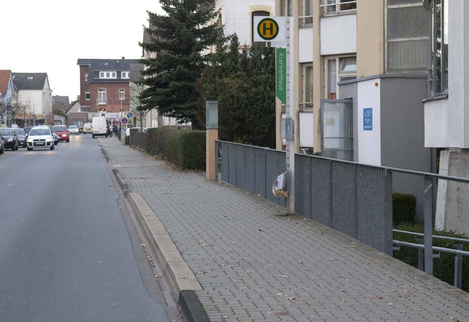 Straße mit Gehweg bei Tag, die Haltestelle ist nur am Schild zu erkennen