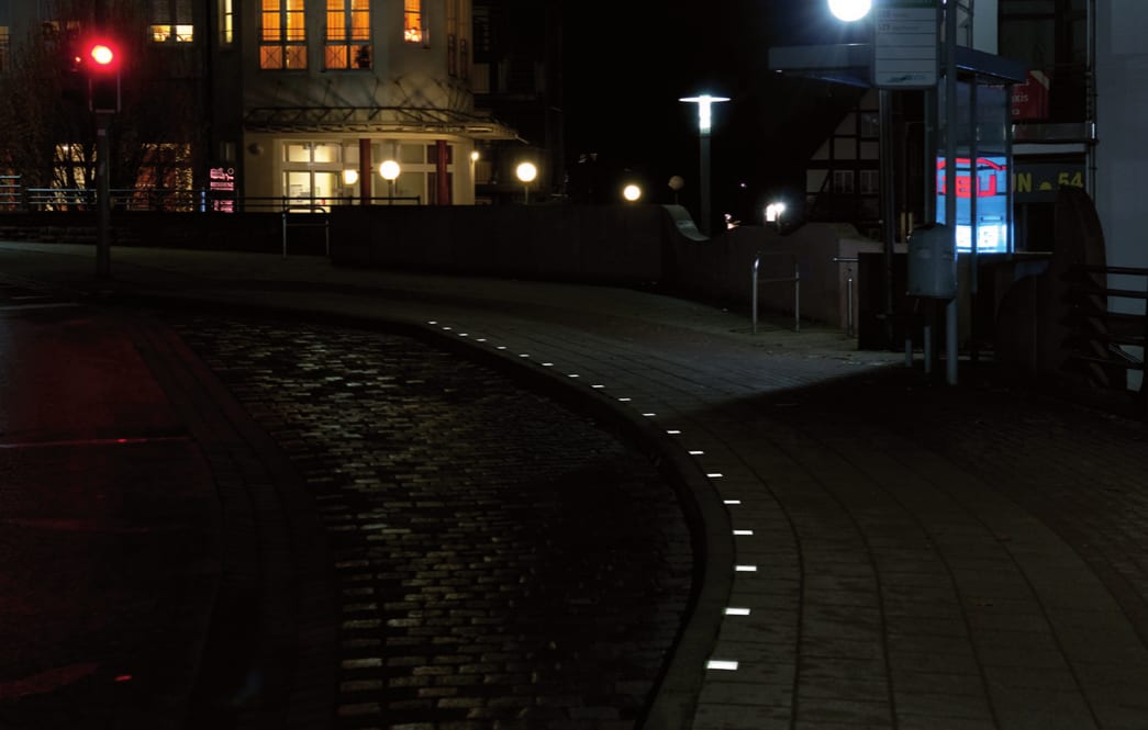 Dieselbe Haltestelle bei Nacht mit einer Leuchtenkette aus Lightstone entlang der Bordkante