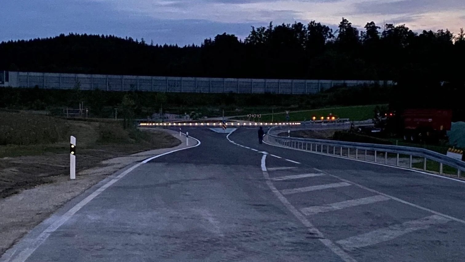 Straße an der Kreisverkehrsausfahrt bei Dämmerung, eine Reihe von Pflasterleuchten folgt dem Bord