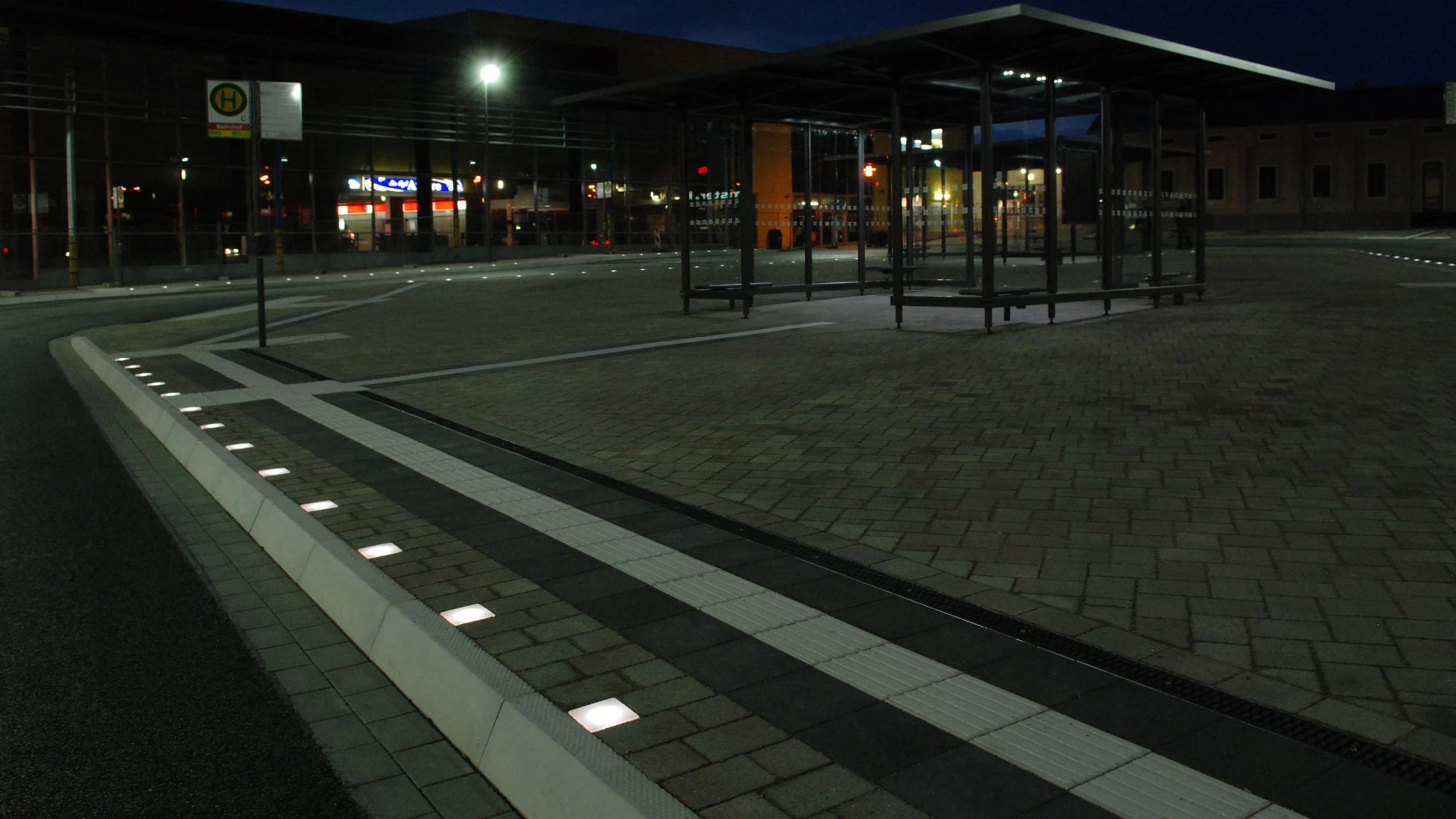 Bahnsteigkante bei Nacht, eine Reihe von Pflasterleuchten zeichnet die Kante nach