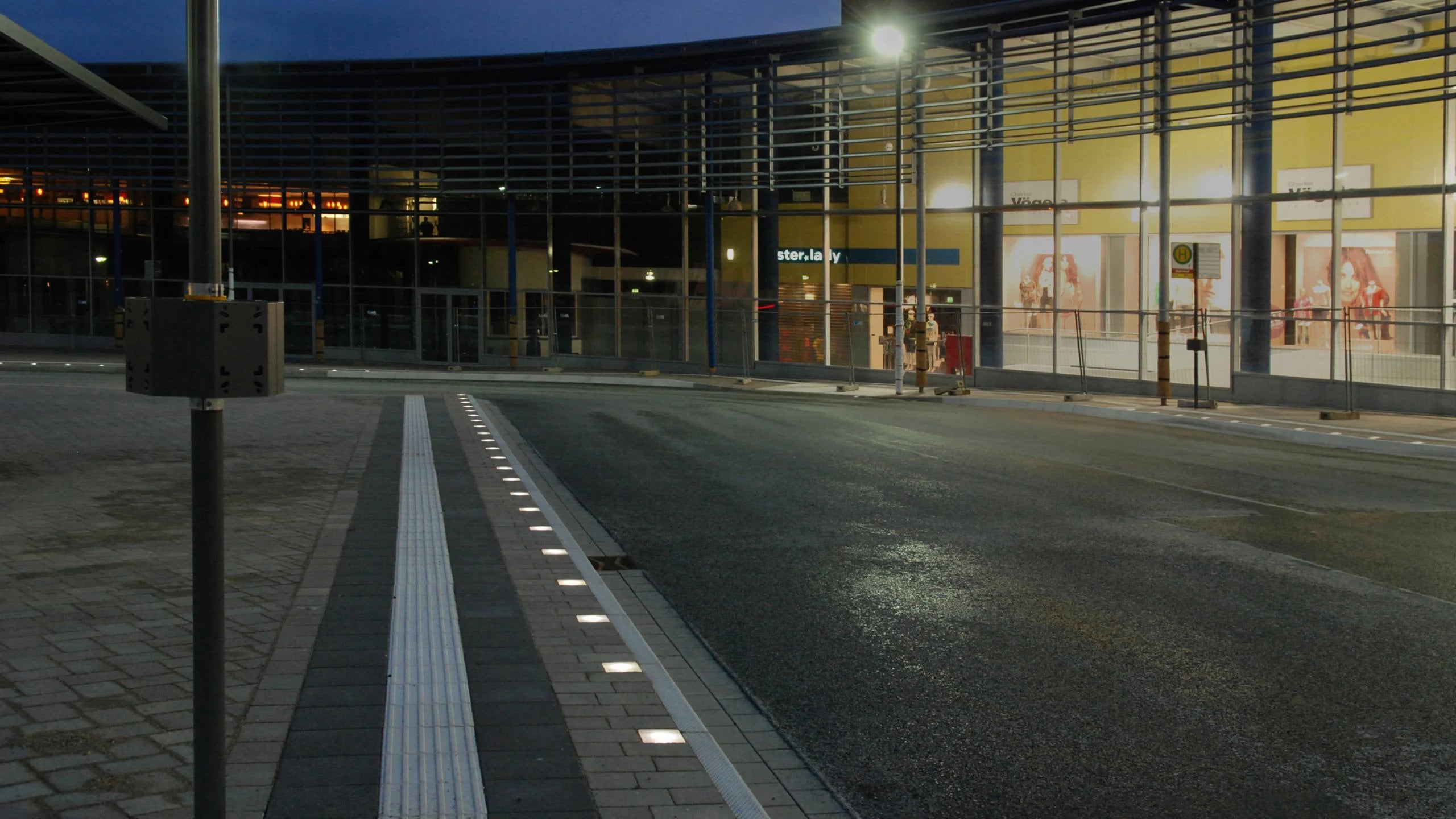 Bus stop at dusk, tactile guidance strip with a line of light in front of a shop front