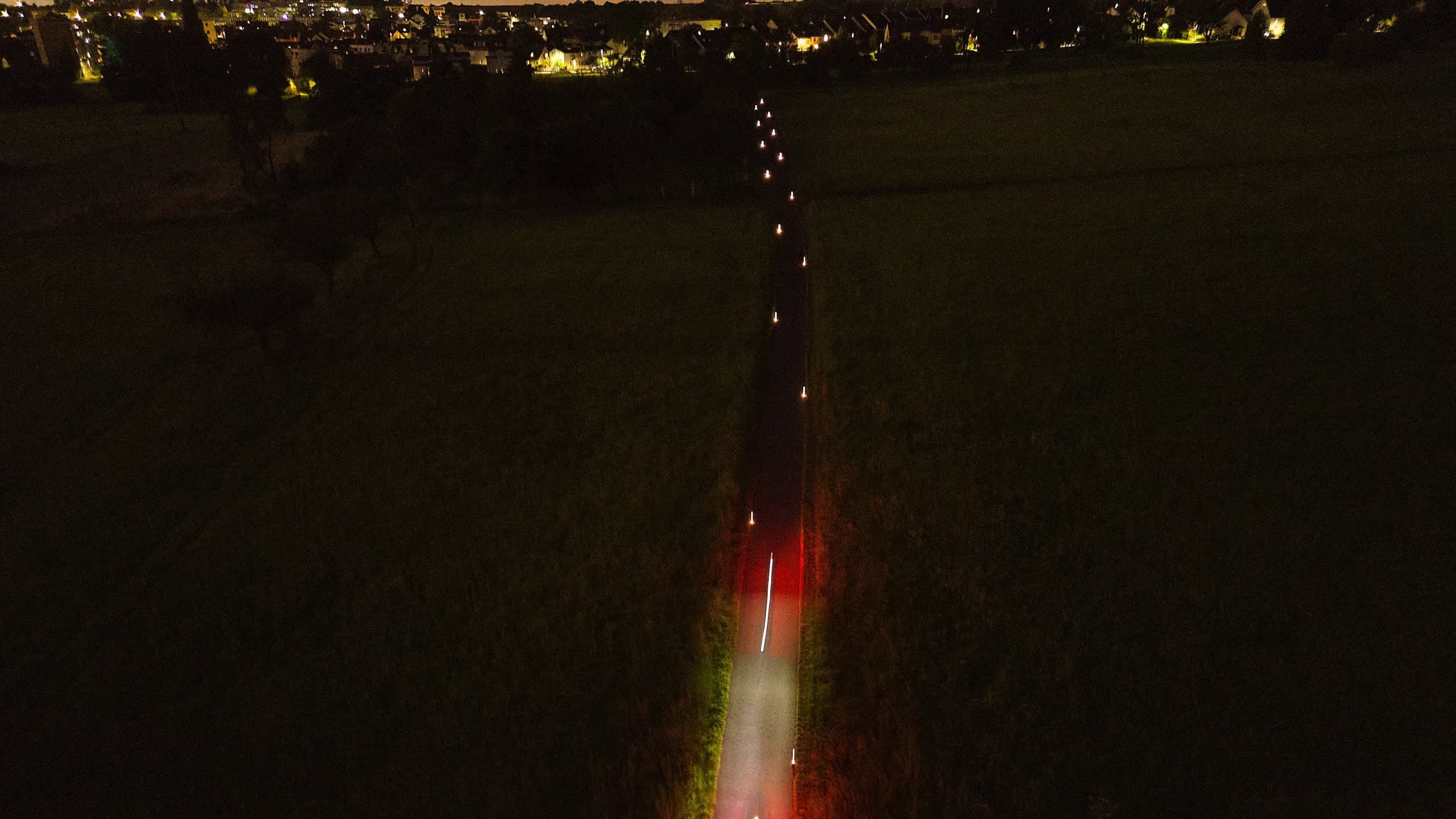 Radweg bei Nacht durch das Feld, Road Studs führen zum Ort, rote Lichtspur eines Fahrrads
