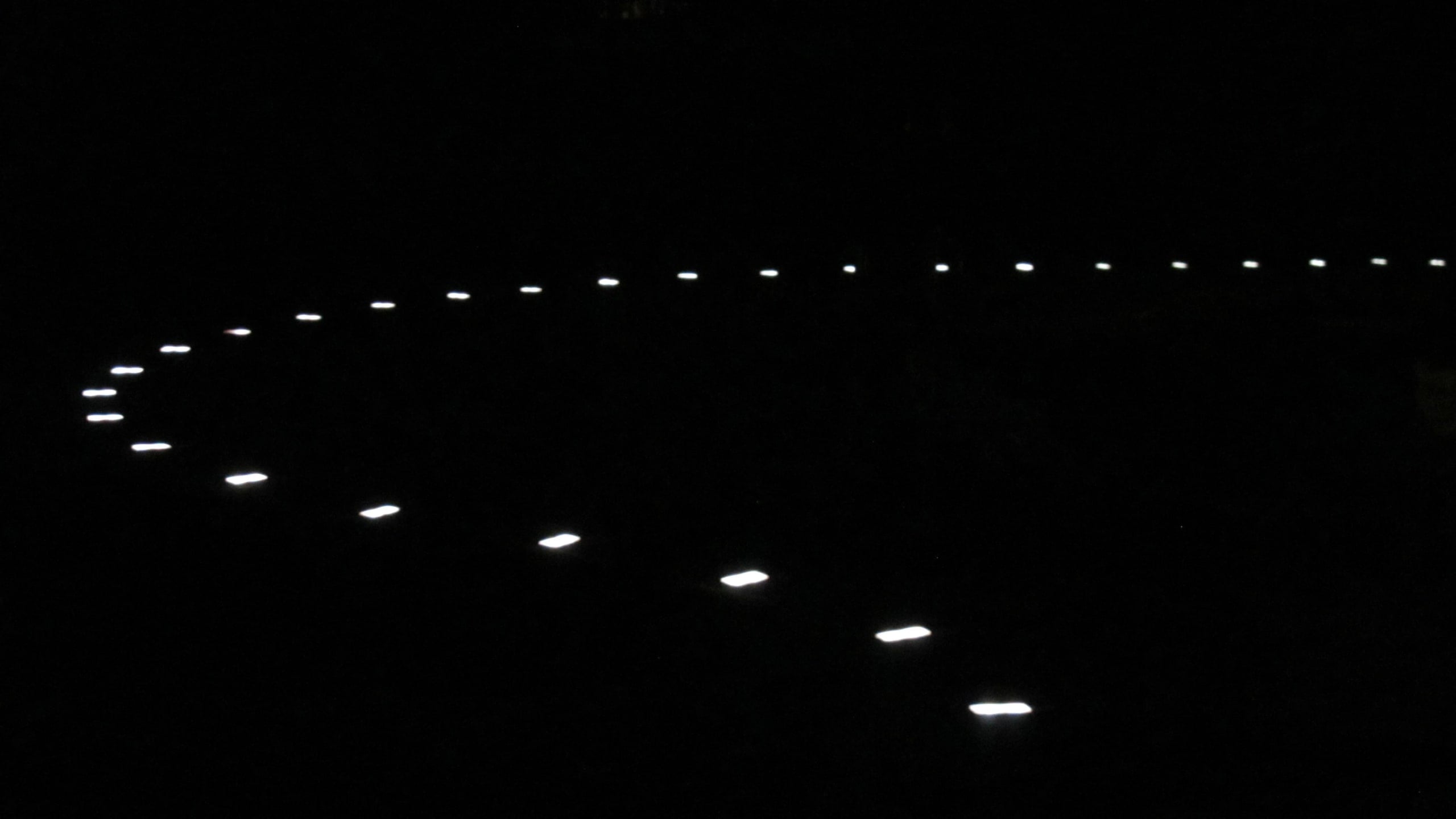Geschwungene Zufahrt in einem Garten bei Nacht, eine Linie leuchtender Steine zeichnet den Bogen nach
