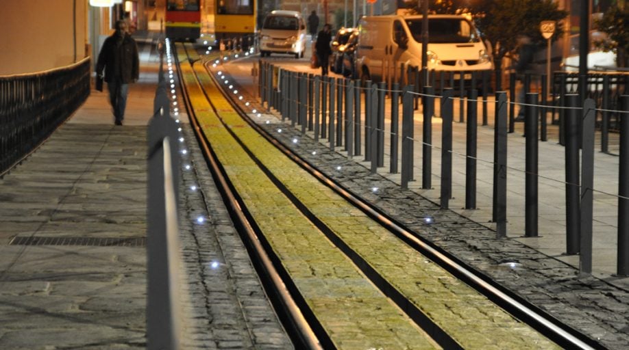 Gleisbereich neben einem Gehweg bei Dämmerung, Road Studs markieren die Trennung