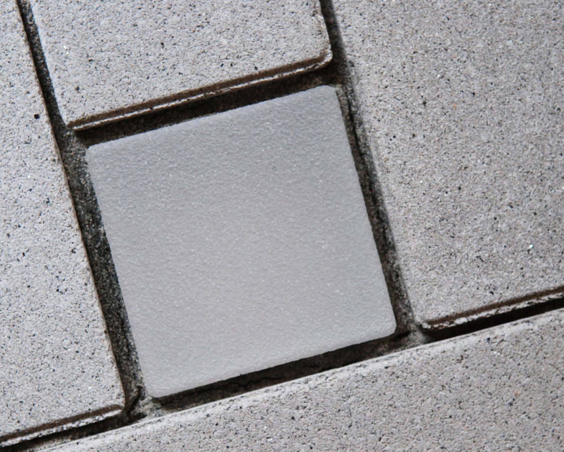 Lightstone LED-Pflasterstein bei Tag, hellgrau zwischen grauen Betonsteinen