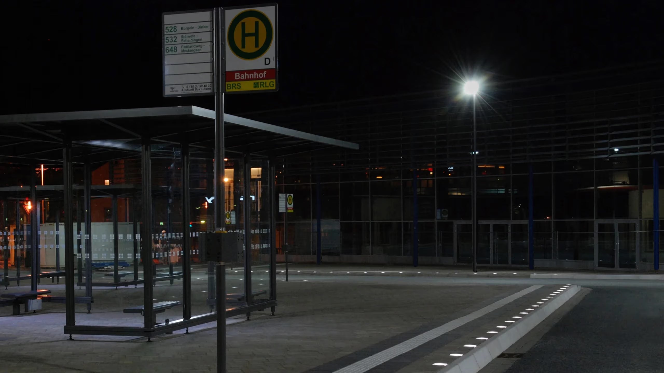 Haltestelle bei Nacht, Haltestellenschild und Unterstand, Lichtlinie am Bord