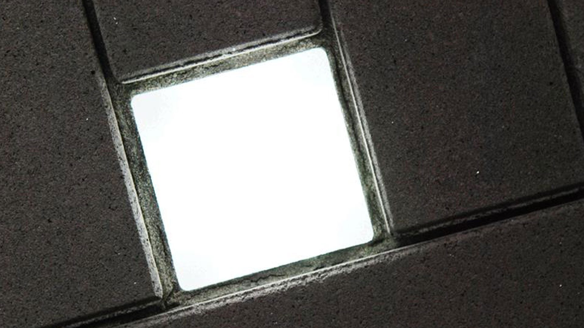 Quadratischer Lightstone LED-Pflasterstein, leuchtend zwischen dunklen Betonsteinen