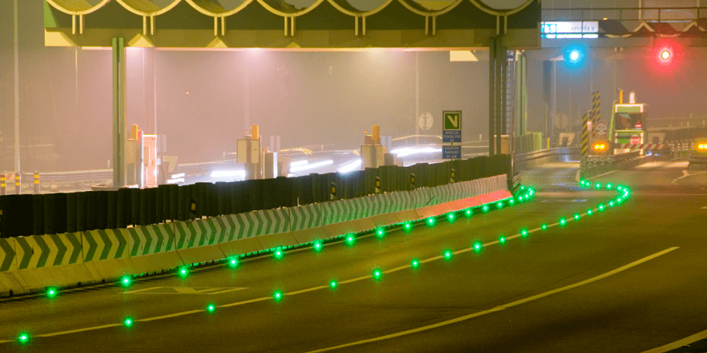 Fahrbahn im Nebel bei Nacht, grün leuchtende Road Studs führen die Fahrstreifen